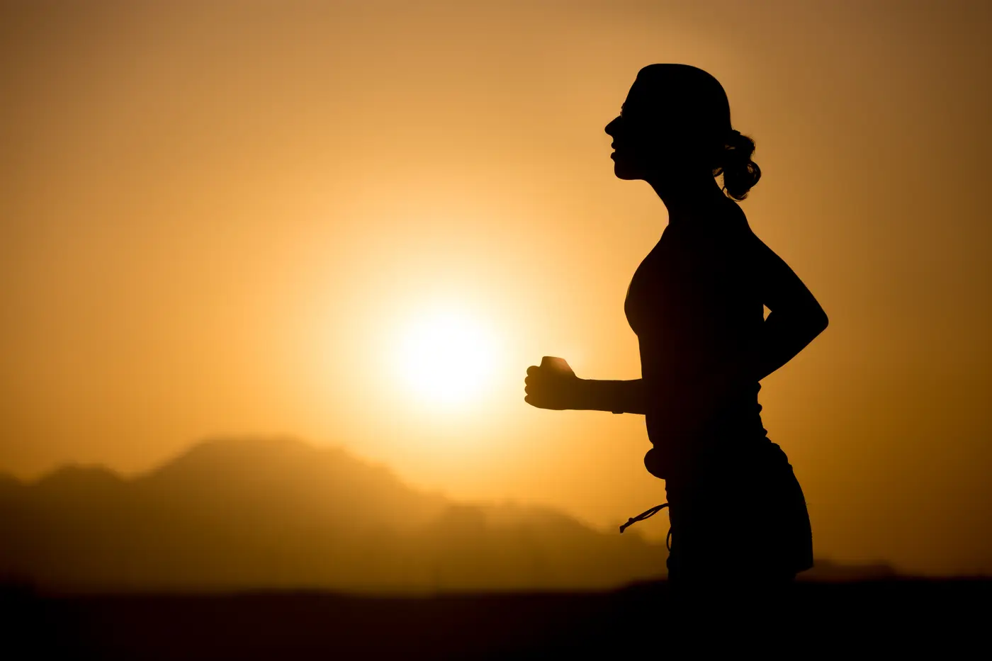 Jogging in mountains Profile silhouette of young sporty woman jogging against colorful picturesque mountainous landscape with rising or setting sun, copy space